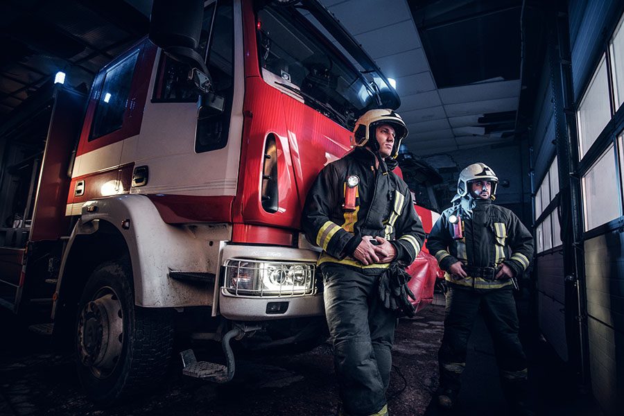 Municipal Workers Compensation Insurance - Portrait of Two Firefighters Standing in Front of Their Fire Truck